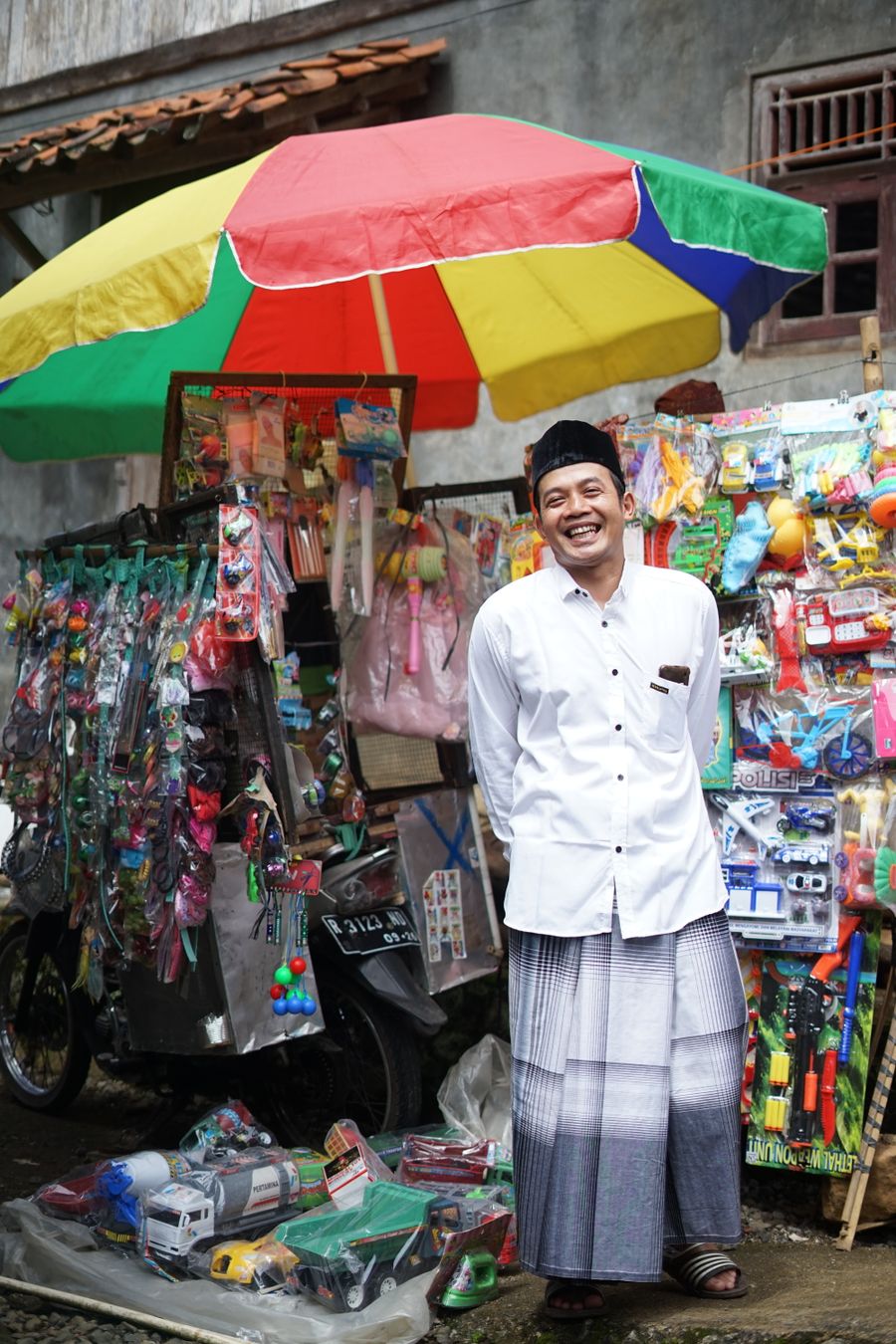 Penjual mainan keliling tersenyum di depan gerobaknya